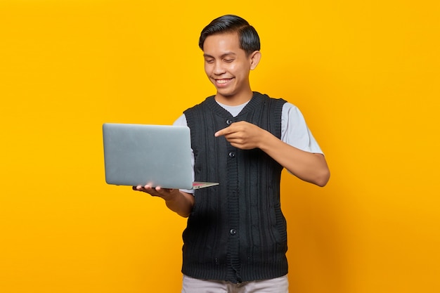 Gai beau jeune homme pointant un ordinateur portable sur fond jaune