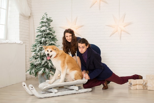 Gai jeune couple sur un traîneau avec un chien dans les décorations de Noël