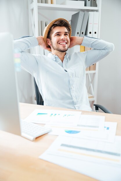 Gai jeune homme au chapeau assis et relaxant au bureau