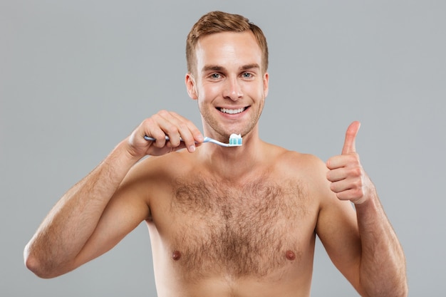 Gai jeune homme tenant une brosse à dents et montrant les pouces vers le haut