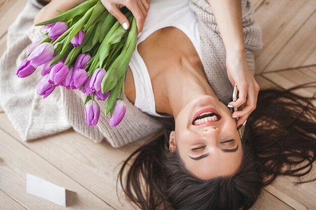 Gaie jeune femme parlant au téléphone et tenant des fleurs. Belle dame aux tulipes