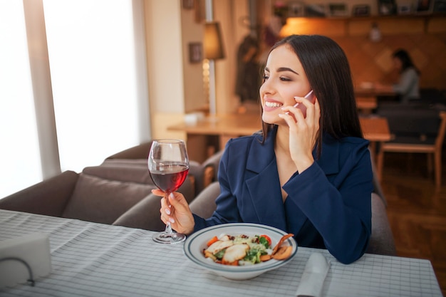 Gaie jeune femme s'asseoir à table et parler au téléphone.