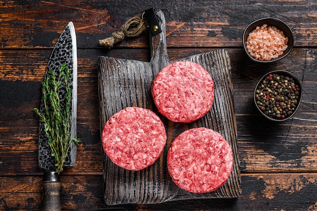 Galettes de burgers de steak cru avec du boeuf haché et du thym sur une planche à découper en bois