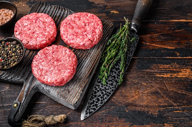 Galettes de burgers de steak cru avec du boeuf haché et du thym sur une planche à découper en bois