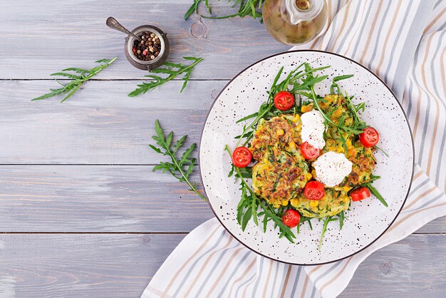 Galettes de courgettes au maïs et à la crème sure, roquette, salade de tomates. Vue de dessus