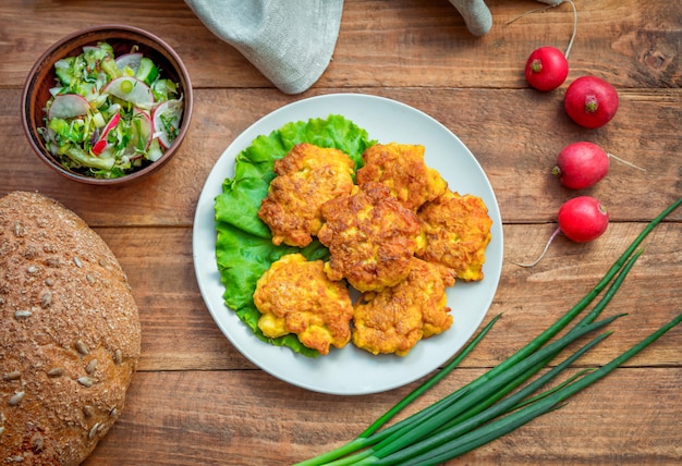 Galettes de poulet maison, servies sur une assiette, salade, pain, oignon vert et radis sur table en bois.