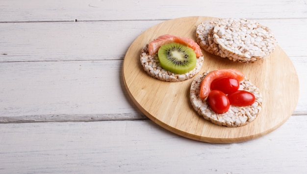 Galettes de riz au saumon, kiwi et tomates cerises sur une table en bois blanche.