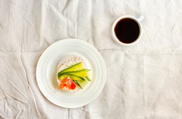 Photo galettes de riz croustillantes à l'avocat et au saumon frais salé. tasse de café. vue de dessus. espace pour le texte. repas riche en protéines et faible en glucides. fond de nappe en lin blanc.