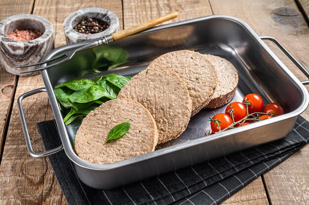 Galettes sans viande crue à base de viande végétale, escalopes de burger végétaliennes fraîches dans un plateau de cuisine avec des herbes. Fond en bois. Vue de dessus.