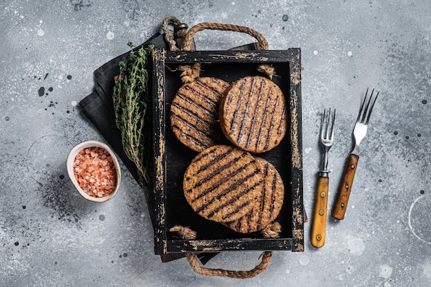 Galettes sans viande rôtie, escalopes de burger de viande à base de plantes dans un plateau en bois avec des herbes. Fond gris. Vue de dessus.