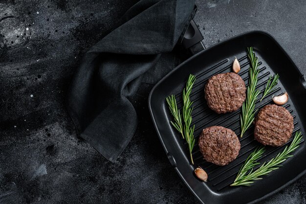 Galettes de viande de hamburger grillées avec des épices sur une lèchefrite. Fond noir. Vue de dessus. Espace de copie.