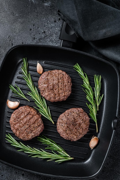 Galettes de viande de hamburger grillées avec des épices sur une lèchefrite. Fond noir. Vue de dessus.