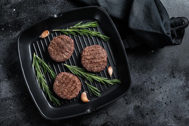 Galettes de viande de hamburger grillées avec des épices sur une lèchefrite. Fond noir. Vue de dessus.