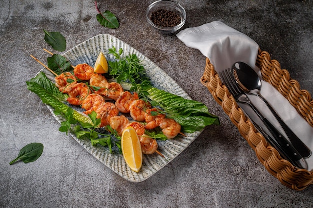 Gambas grillées au citron et aux herbes sur une assiette contre une table en pierre grise, brochette de poisson