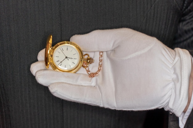 Un gant blanc tient une montre de poche en or avec le numéro 12 dessus.