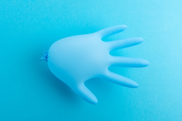 Gant médical en latex bleu sur fond bleu pastel.