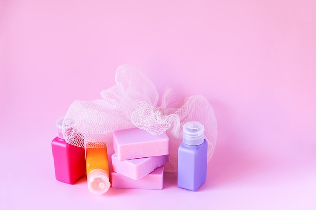 Gant de toilette coloré, petites bouteilles de voyage en plastique et barres de savon sur fond rose tendre. Ensemble d'accessoires pour les soins du corps et l'hygiène.