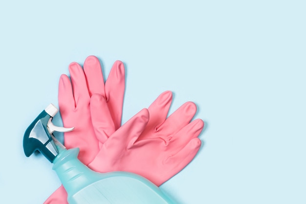 Gants en caoutchouc rose et pulvérisateur de produit de nettoyage sur fond bleu clair