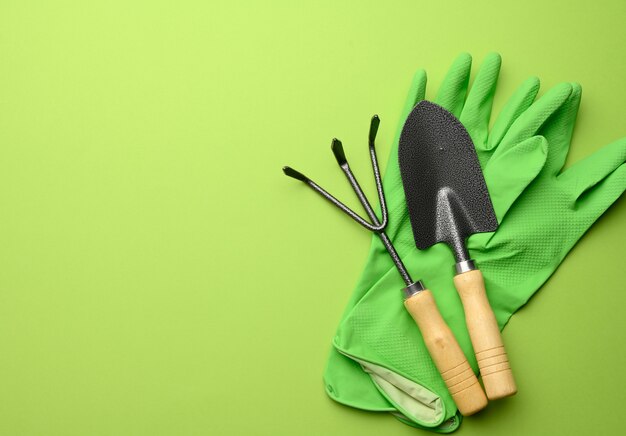 Gants en caoutchouc vert et ensemble de jardin de pelles, râteaux, fourches sur fond vert, vue du dessus, mise à plat