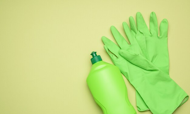 Gants en caoutchouc vert pour nettoyer et nettoyer le liquide dans une bouteille en plastique sur fond vert, à plat, copiez l'espace