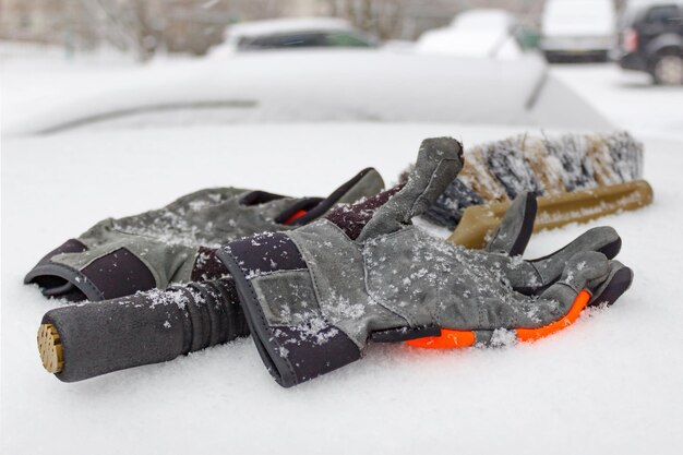Gants d'hiver et brosse à neige sur le toit de voiture couvert de neige