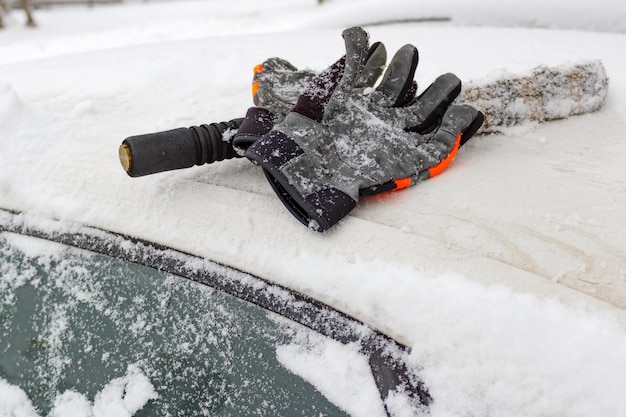 Gants d'hiver et brosse à neige sur le toit de voiture couvert de neige