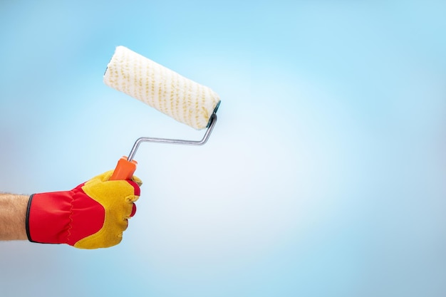 en gants de main tenant une brosse à rouleaux sur fond bleu avec un endroit pour le texte Concept de rénovation à la maison