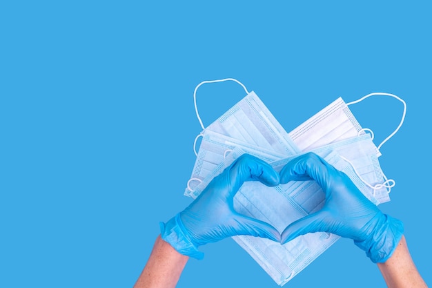 Gants médicaux bleu symbole de la main en forme de coeur sur les masques de protection médicale en forme de coeur sur bleu