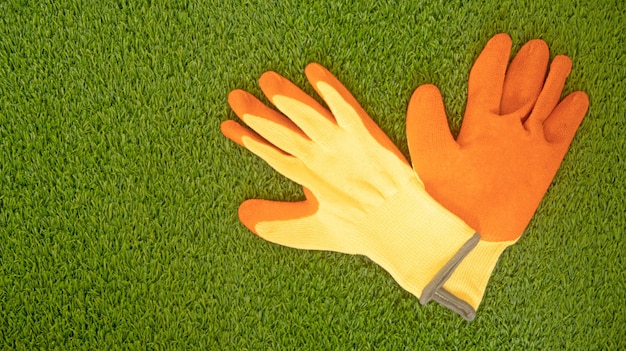 GANTS DE TRAVAIL ORANGE ET JAUNE SUR UN FOND D'HERBE VERTE AVEC DES OUTILS