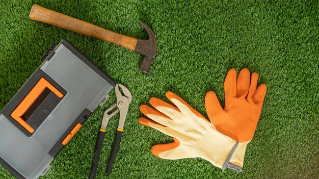 GANTS DE TRAVAIL ORANGE ET JAUNE SUR UN FOND D'HERBE VERTE AVEC DES OUTILS