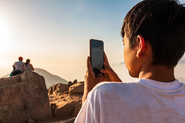 Garçon de 14 ans avec un téléphone portable à la main essayant d'envoyer un message texte depuis une montagne