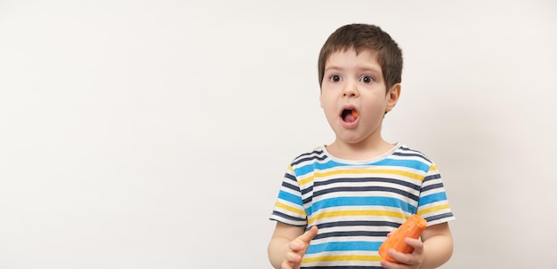 Un garçon de 4 ans mange des carottes sur fond blanc