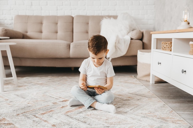 Un garçon de 5 ans regarde un smartphone l'enfant est assis par terre et tient le téléphone