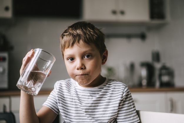 Garçon de 6 ans de l'eau potable du verre assis à la table