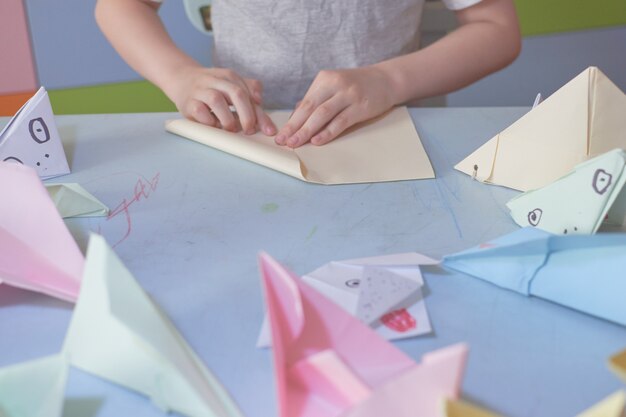 Un garçon de 6 ans fabrique des avions et des grenouilles en origami pendant la quarantaine Covid-19, l'auto-isolement, le concept d'éducation en ligne, l'enseignement à domicile. Enfant à la maison, jardin d'enfants fermé, art pour enfants.