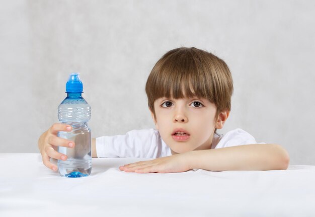 Garçon de 6 ans vêtu d'une chemise blanche boit de l'eau