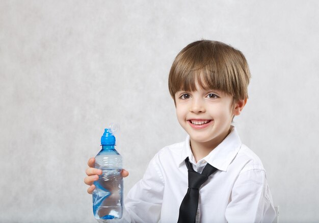 Garçon de 6 ans vêtu d'une chemise blanche boit de l'eau