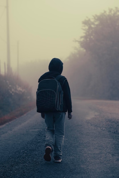 Un garçon de 8 ans avec un sac à dos va à l'école le long d'une route de campagne le matin seul au printemps