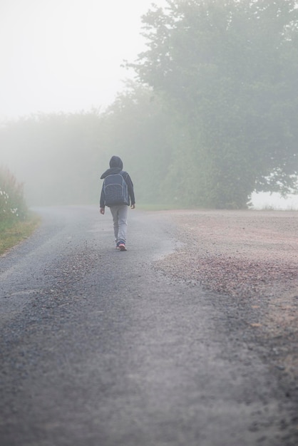 Un garçon de 8 ans avec un sac à dos va à l'école le long d'une route de campagne le matin seul au printemps