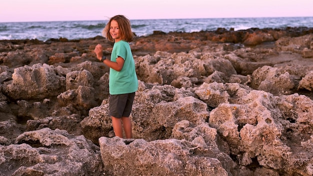 Un garçon de 9 ans aux longs cheveux clairs saute agilement le long du bord de mer rocheux en explorant chaque recoin