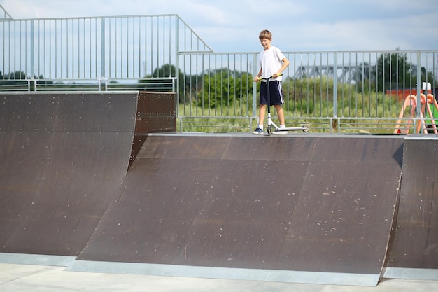 Photo un garçon actif de dix ans sur un scooter dans le parc de skate d'été