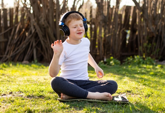 Garçon adolescent aux cheveux roux en T-shirt blanc avec les yeux fermés écoutant de la musique sur une tablette mobile
