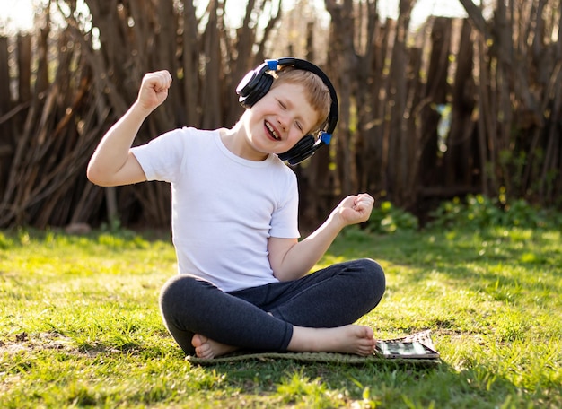 Garçon adolescent aux cheveux roux en T-shirt blanc avec les yeux fermés écoutant de la musique sur une tablette mobile