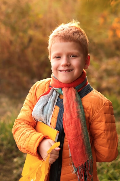 Garçon adolescent drôle aux cheveux roux souriant regardant la caméra tenant un livre, feuille tombée jaune à la main