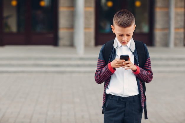 Garçon adolescent écolier avec téléphone portable debout à l'école sur fond