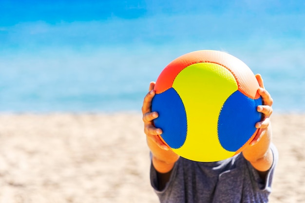 Photo garçon adolescent jouant avec ballon sur la plage en journée ensoleillée