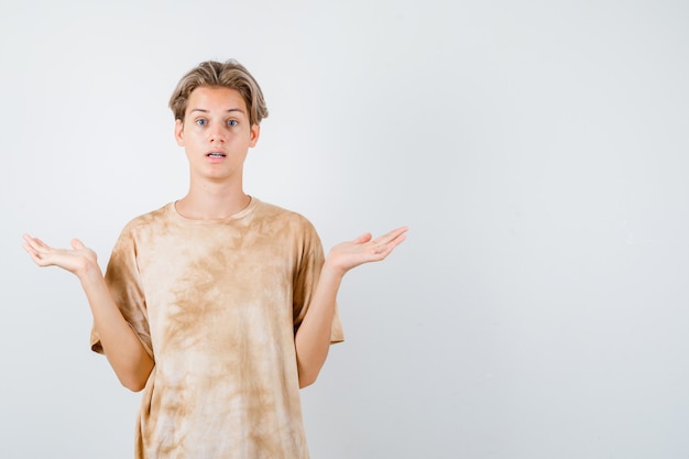 Garçon adolescent montrant un geste impuissant en t-shirt et l'air perplexe, vue de face.