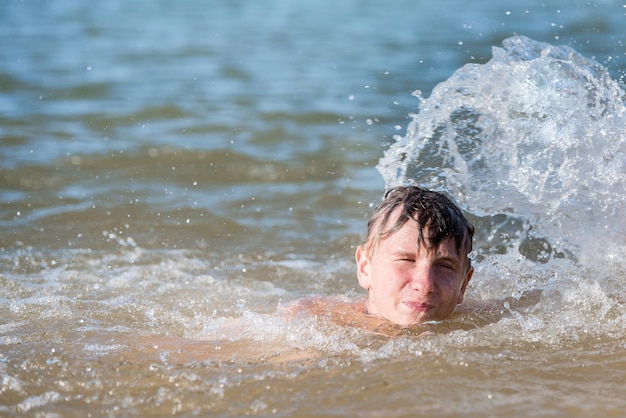 Un garçon adolescent nage dans un jet d'eau un concept de vacances à la plage