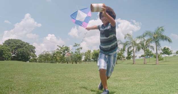 Garçon africain essayant de faire voler un cerf-volant dans le parc. Concept d'activité de vacances.