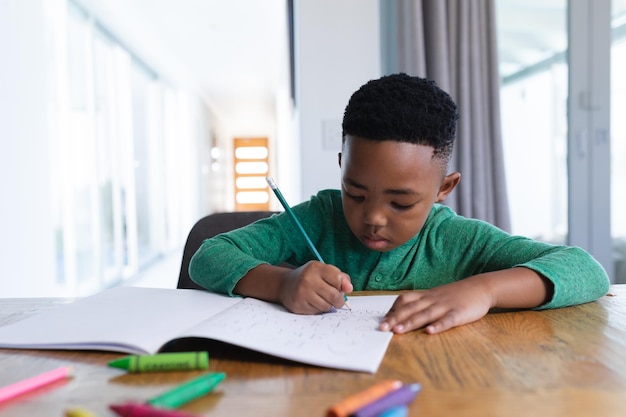 Garçon afro-américain dans une classe d'école en ligne, écrivant dans son cahier
